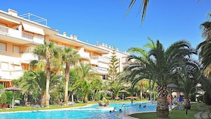A swimming pool surrounded by palm trees and a multi-story building with balconies. - Nou Fontana by Interhome (Jávea)