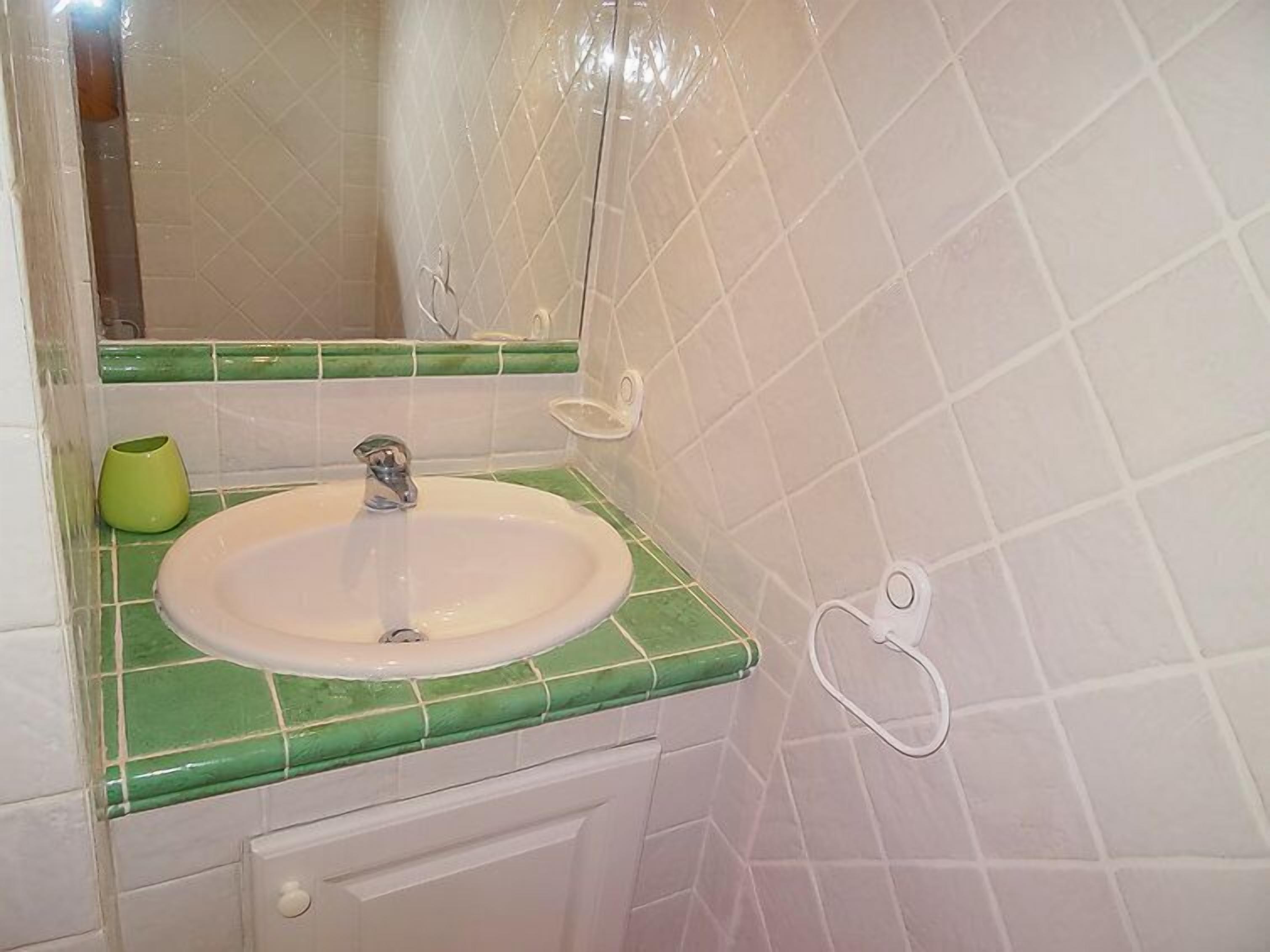 A bathroom with a white sink, green-tiled countertop, and a mirror.