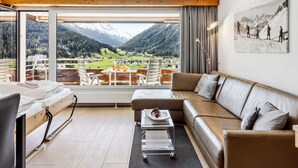 A modern hotel room with a large window offering a mountain view, a sofa, a dining table, and a bed. - Guardaval Apt 602 by Interhome (Davos)