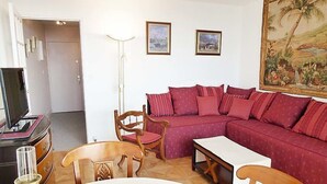 Un salon avec un canapé rouge, des chaises en bois, une table blanche et un téléviseur posé sur un meuble.