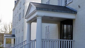 Un bâtiment blanc doté d’un porche soutenu par des colonnes, d’un escalier et d’une porte avec des volets.