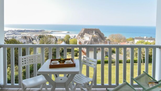 Un balcon avec une table et des chaises, offrant une vue sur la côte, avec des bâtiments et la mer.