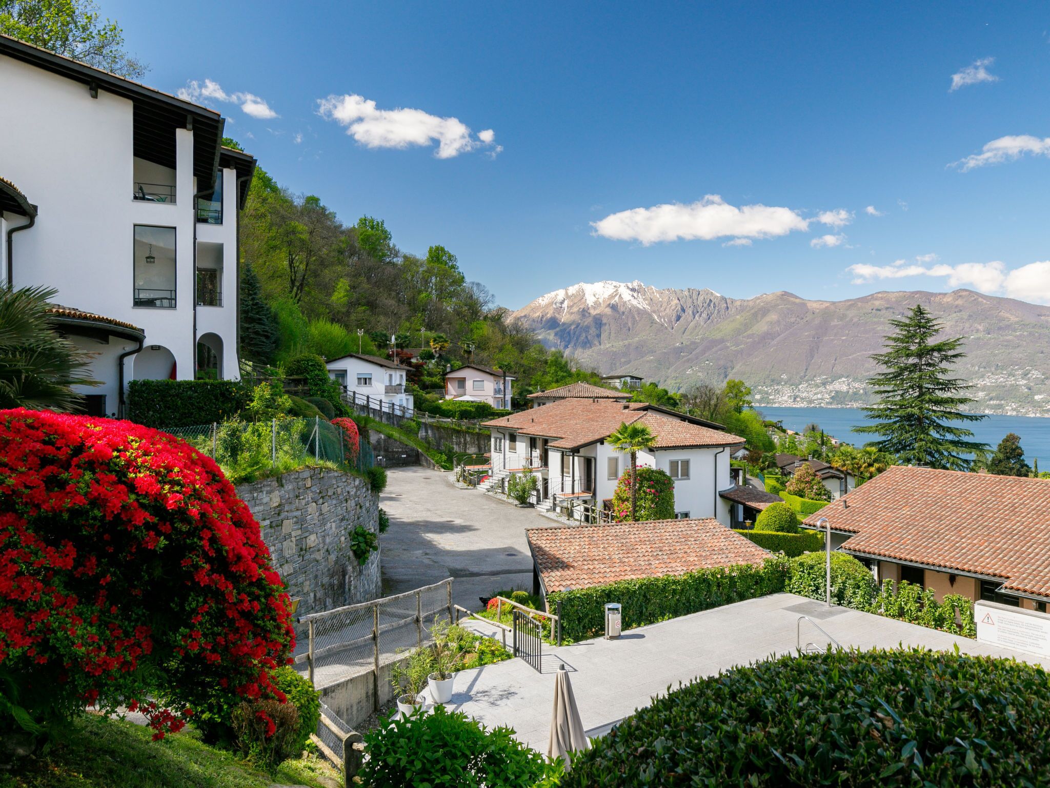 Una zona residencial en una ladera con casas, un muro de piedra y vistas a un lago y montañas.