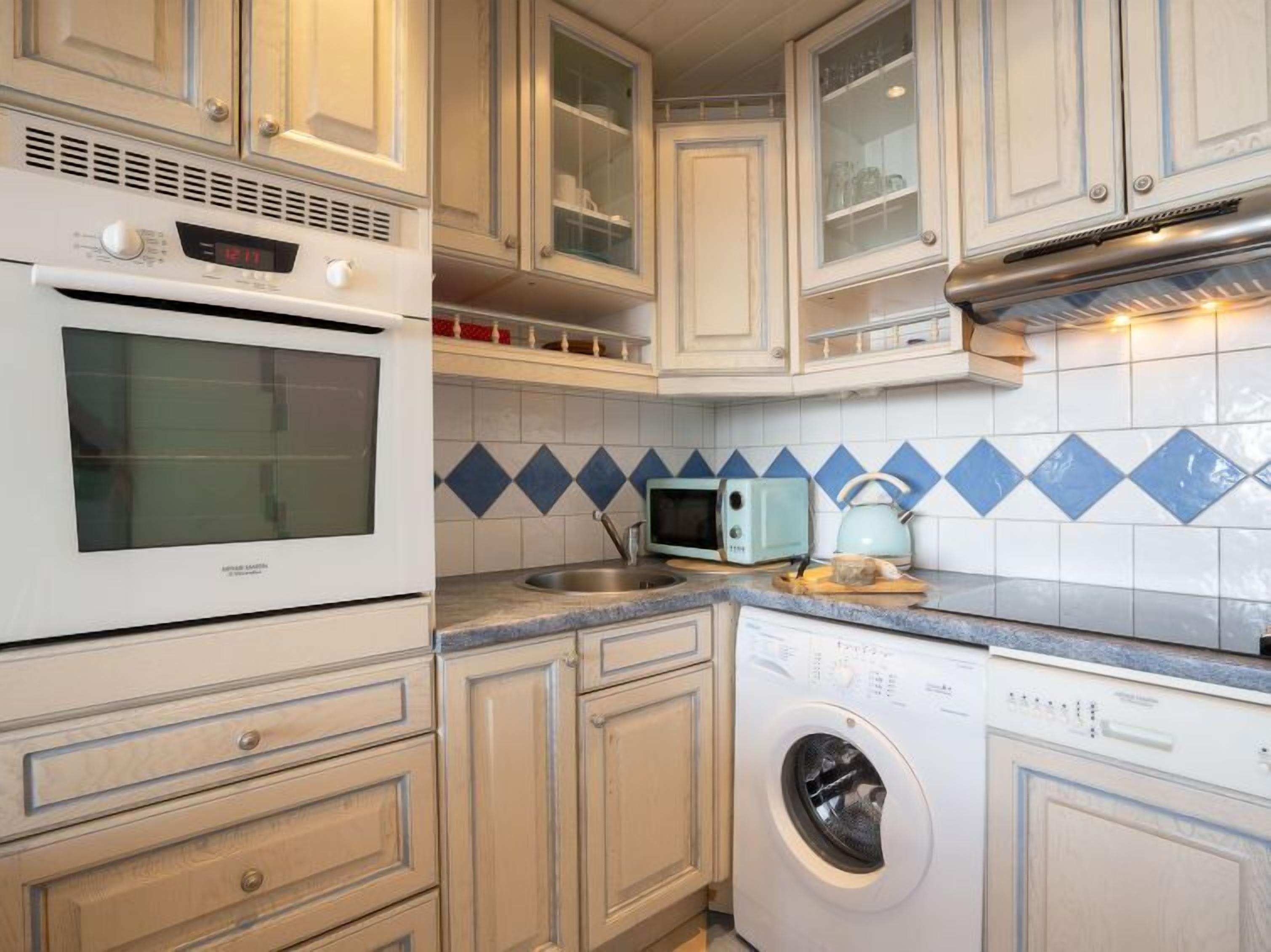 A compact kitchen with white cabinetry, a built-in microwave, a washing machine, and a sink.