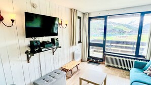 A living room with a TV, speakers, a bench, a table, and a sofa. - Le Slalom (Val Claret) by Interhome (Tignes)