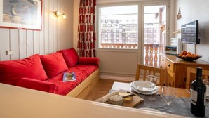 A compact living space with a red sofa, a dining table with a wine bottle, and a TV on the wall. - Le Hameau du Borsat (Val Claret) by Interhome (Tignes)