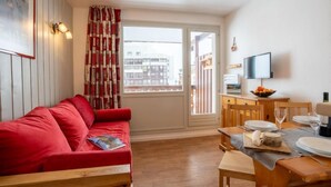 A cozy room with a red sofa, wooden dining table, and a TV. - Le Hameau du Borsat (Val Claret) by Interhome (Tignes)