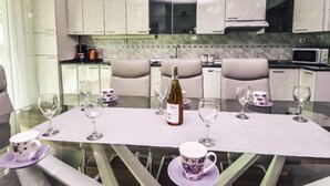Uma cozinha moderna com armários brancos, uma mesa de jantar de vidro e uma garrafa de vinho.