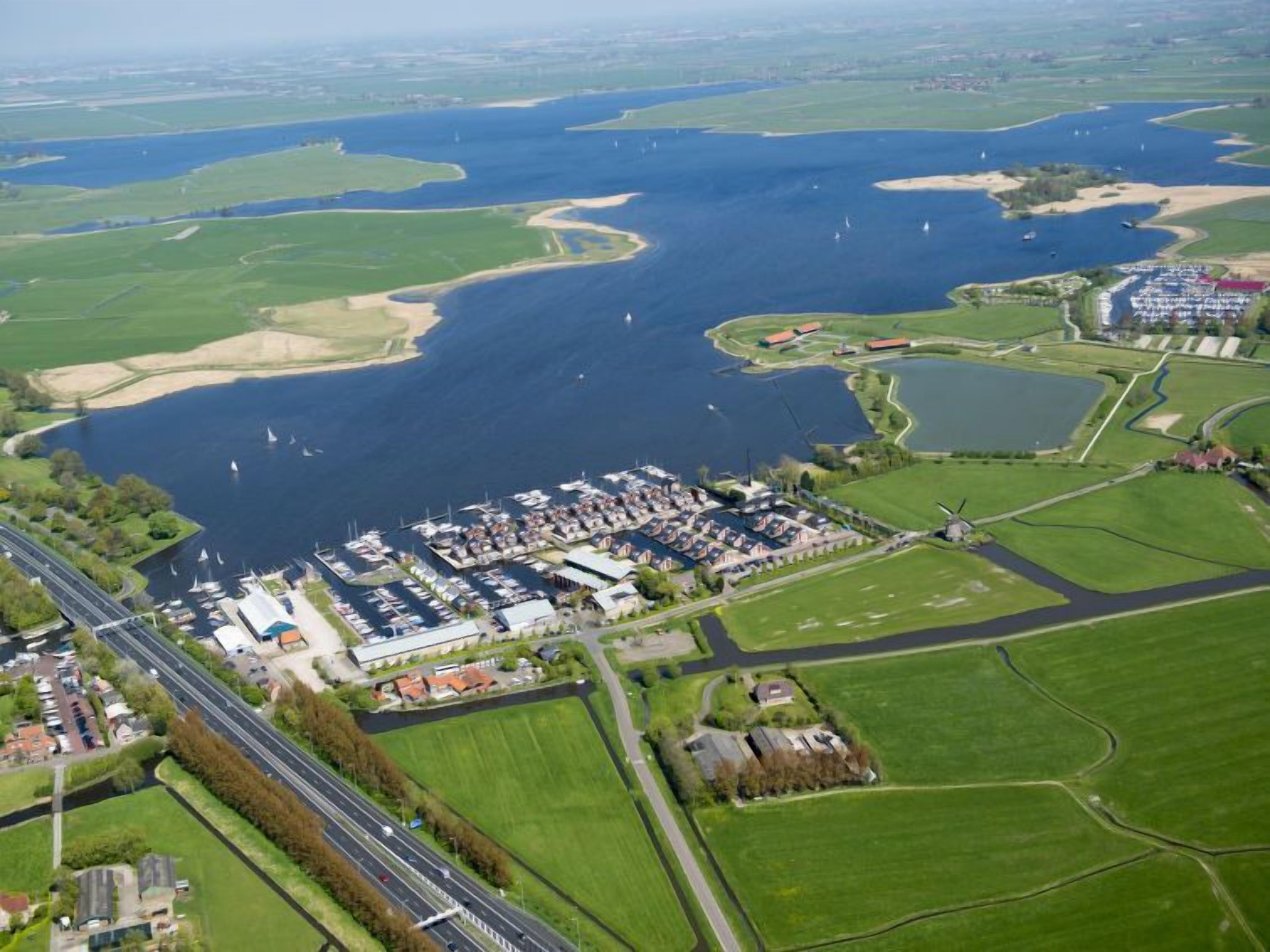 Oversigtsbillede af en lysthavn med både, parkeringsplads og grønne marker i nærheden.