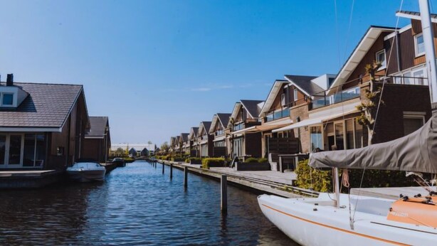 A canal with modern houses on one side and a boat docked on the other. - Vacation home Assum by Interhome (Uitgeest)