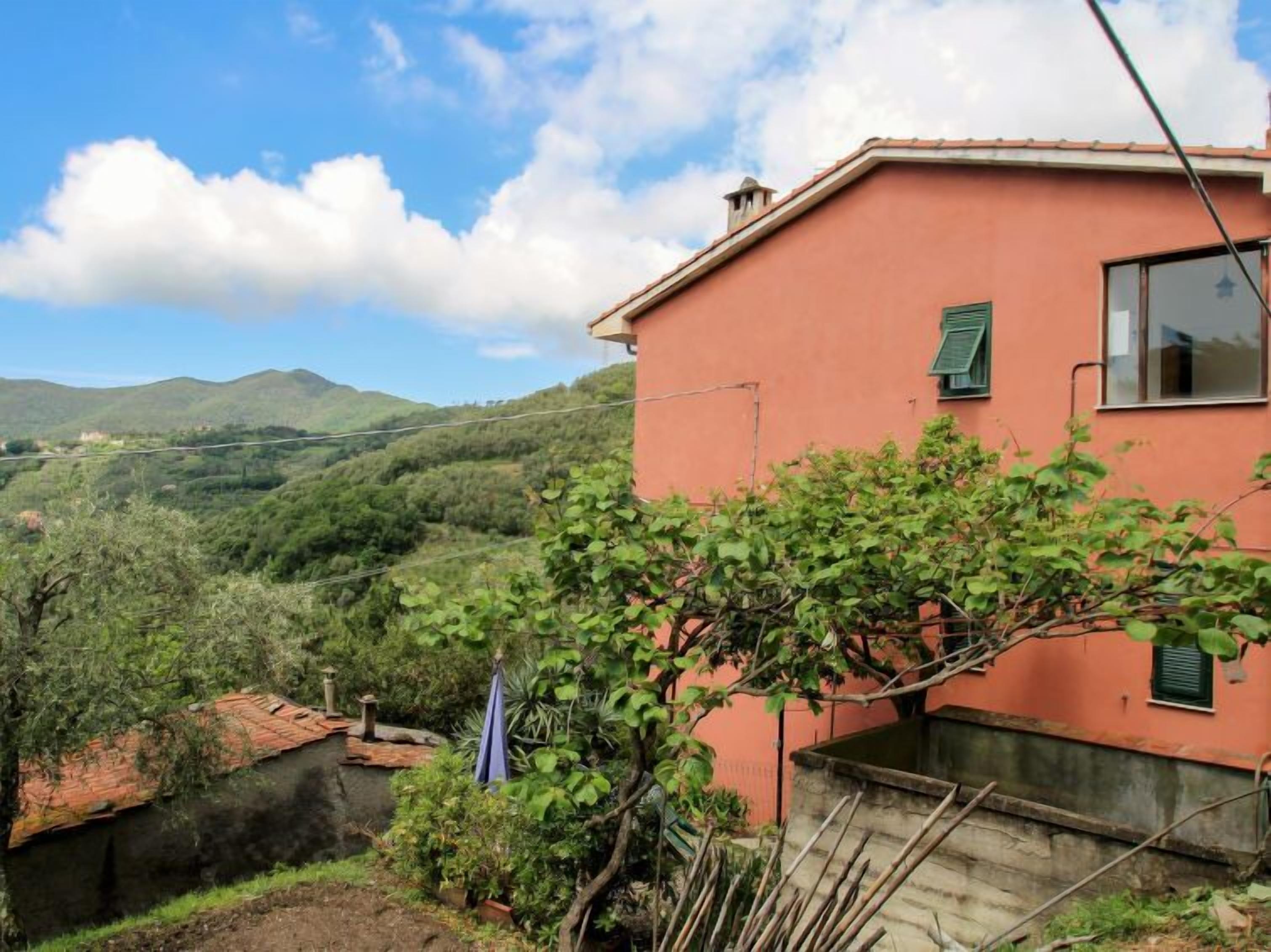 Une maison de plain-pied à l’extérieur rouge, dotée d’un petit balcon et offrant une vue sur une vallée verdoyante et des collines.
