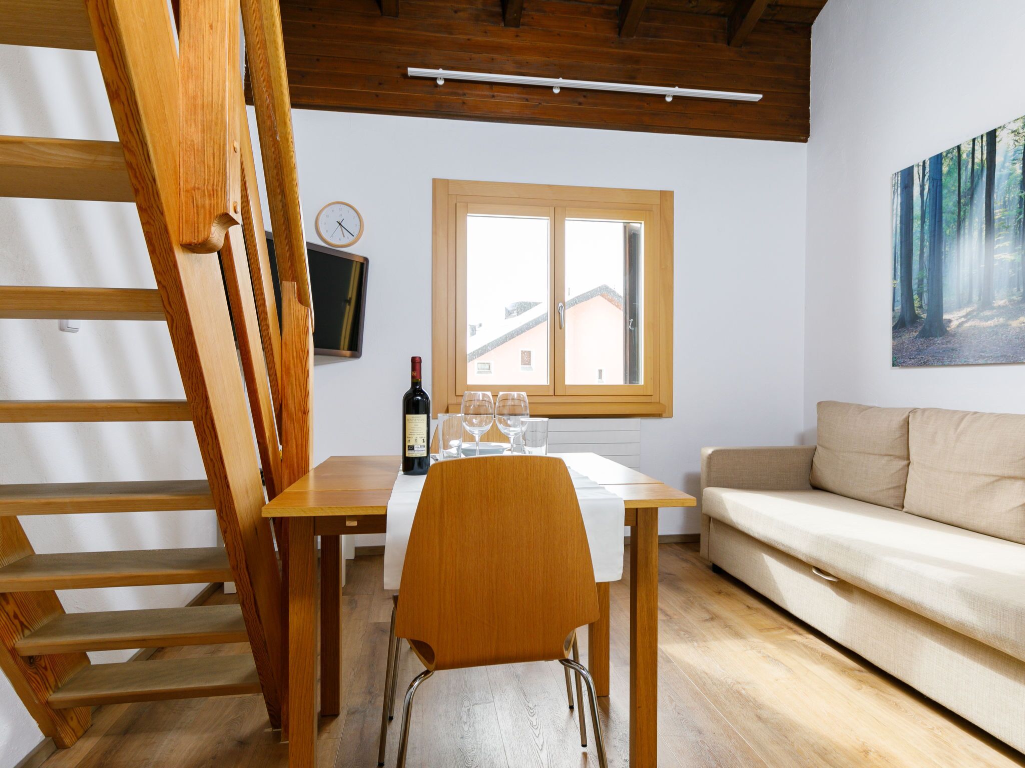 Eine Holztreppe, ein Esstisch mit Weingläsern, ein Sofa und ein Fenster mit Blick auf Gebäude.
