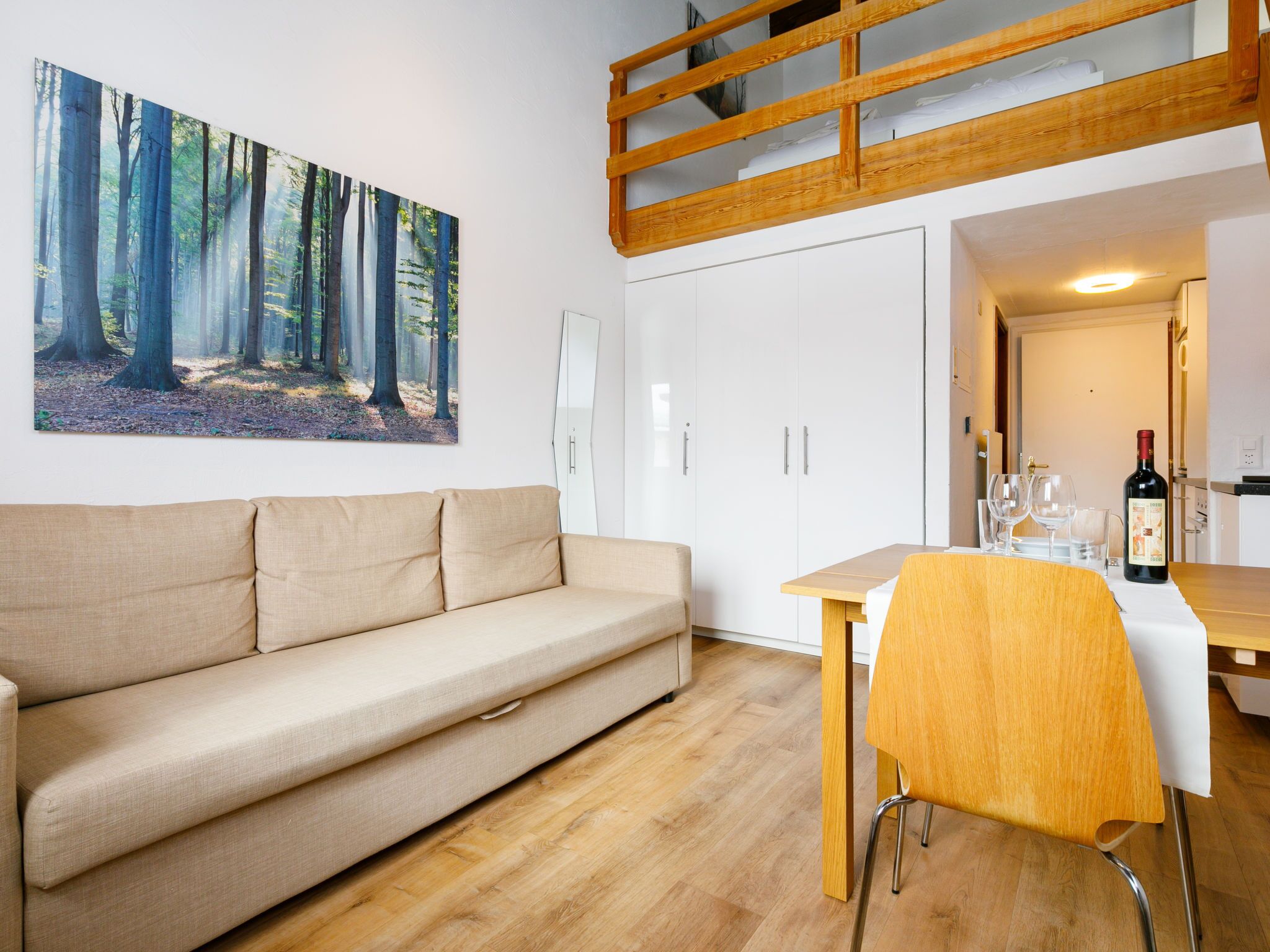 A modern living room with a beige sofa, a dining table with two chairs, and a kitchen area with a wooden ceiling.