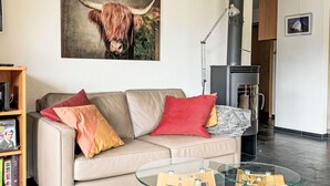 Ein modernes Wohnzimmer mit einem beigefarbenen Sofa, bunten Kissen, einem Glastisch, einem Kamin und einem gerahmten Kunstwerk von einem Stier.