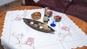 Een ronde houten tafel met een witte tafelkleed waarop tekeningen van uilen staan, een houten dienblad in de vorm van een boot met kaarsen, een fles champagne en schalen met aardbeien en noten.