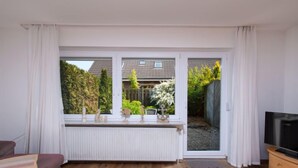Een woonkamer met een groot raam, een radiator, een bank en een tv-meubel.
