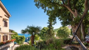 Un bâtiment de style méditerranéen, doté d’un chemin bordé de pierres, d’une végétation luxuriante et offrant une vue sur la mer.