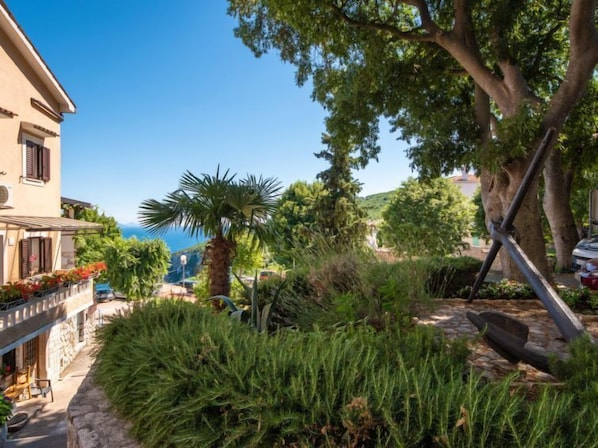 Un edificio de estilo mediterráneo con un sendero de piedra, abundante vegetación y vista al mar.