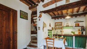A rustic kitchen with a wooden table set for dining, a staircase leading to another level, and a green curtain covering the window. - Il Metatino by Interhome (Camaiore)