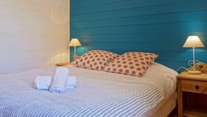 Ein ordentlich bezogenes Bett mit einer gestreiften Decke, zwei Kissen mit rotem Muster und je eine Nachttischlampe auf Holz-Nachttischen.