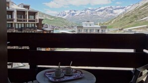 Ein Balkon mit einem für zwei Personen gedecktem Tisch, mit Blick auf eine gebirgige Landschaft und Gebäude in der Ferne.