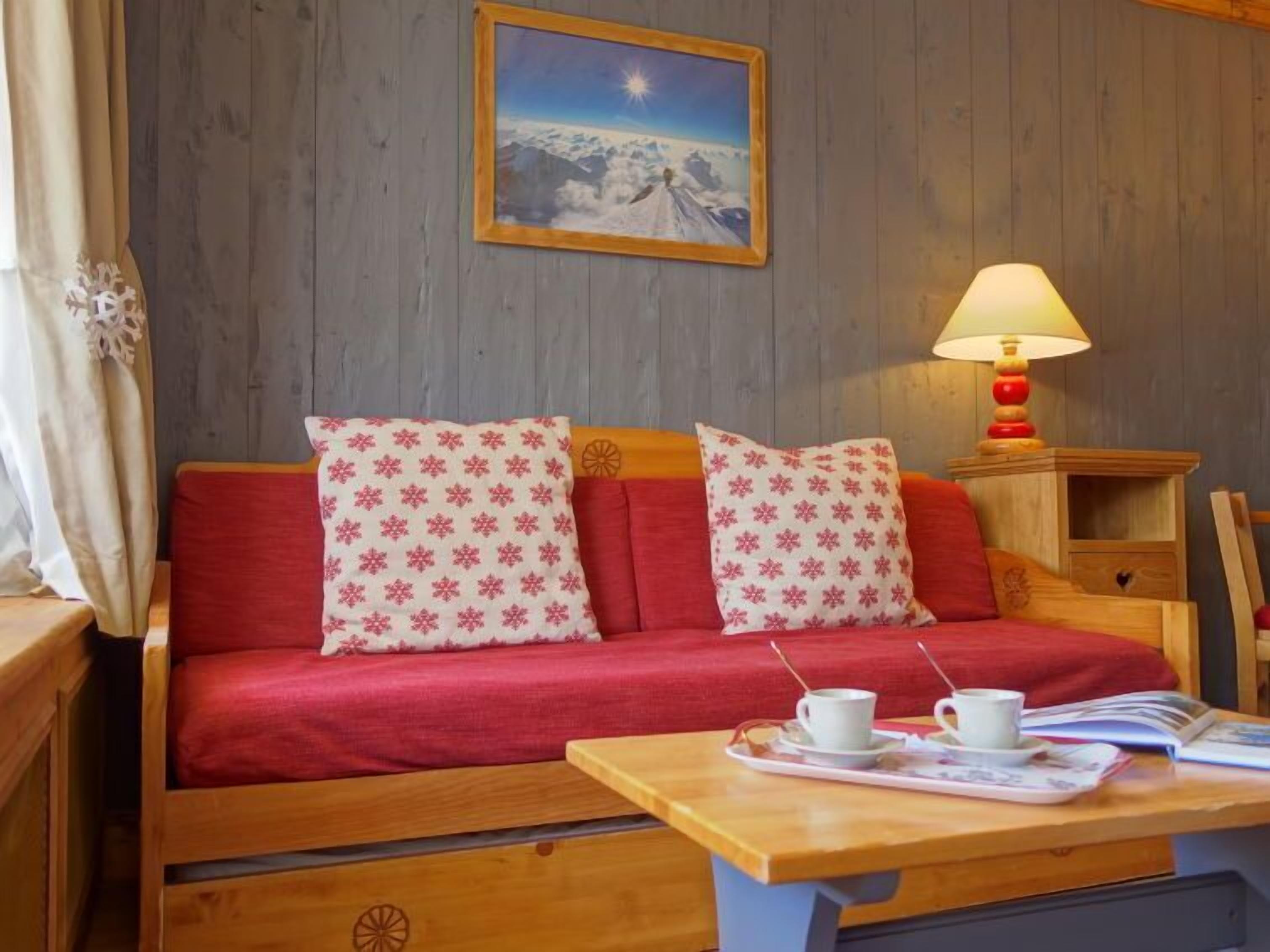 A cozy room with a wooden sofa, two patterned pillows, a table with a tray of cups, and a lamp.