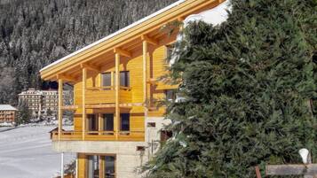 Eine Holzhütte mit Balkon vor einer verschneiten Bergkulisse.