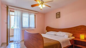 A bedroom with a wooden bed, a ceiling fan, a nightstand with a lamp, and a window with sheer curtains. - Apartment Delfin by Interhome (Karlobag)
