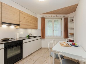 A modern kitchen with a stove, oven, and white cabinets. There is a dining table with chairs and a window with curtains.