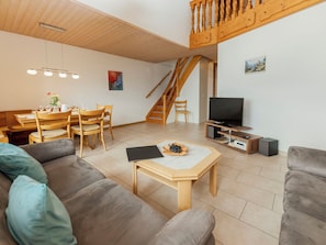 A modern living room with a sofa, a dining table with chairs, a TV, and a staircase.