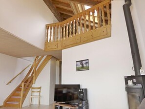 A spacious living area with a wooden staircase, a flat-screen TV, a speaker, and a fireplace. - Apartment Rehli by Interhome (Beatenberg)