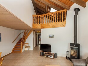 A spacious living area with a wooden staircase, a television, and a wood-burning stove.