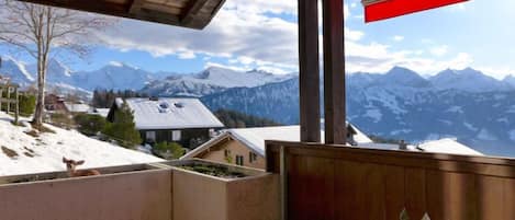A balcony with a wooden floor, a red umbrella, and a view of snow-covered mountains.