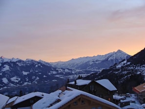 Un village de montagne aux maisons recouvertes de neige, offrant une vue sur des sommets enneigés.