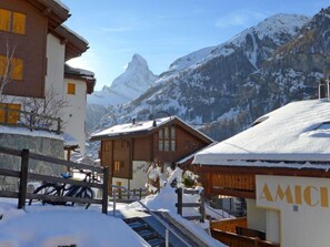 A snow-covered mountain village with wooden buildings, a prominent mountain peak in the background, and a sign reading "AMICI". - Susanna by Interhome (Zermatt)
