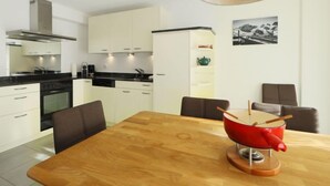 Una cocina moderna con armarios blancos, encimera negra y una mesa de comedor de madera. Hay una olla roja sobre la mesa y una lámpara colgante arriba.