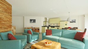 Una sala de estar moderna con sofás color turquesa, una mesa de centro de madera y una cocina al fondo.