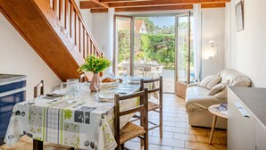A dining area with a table set for two, a wooden staircase, and a view of the garden through glass doors. - Vacation home Sicard by Interhome (Mimizan)