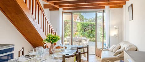 A dining area with a table set for two, a wooden staircase, and a view of the garden through glass doors.