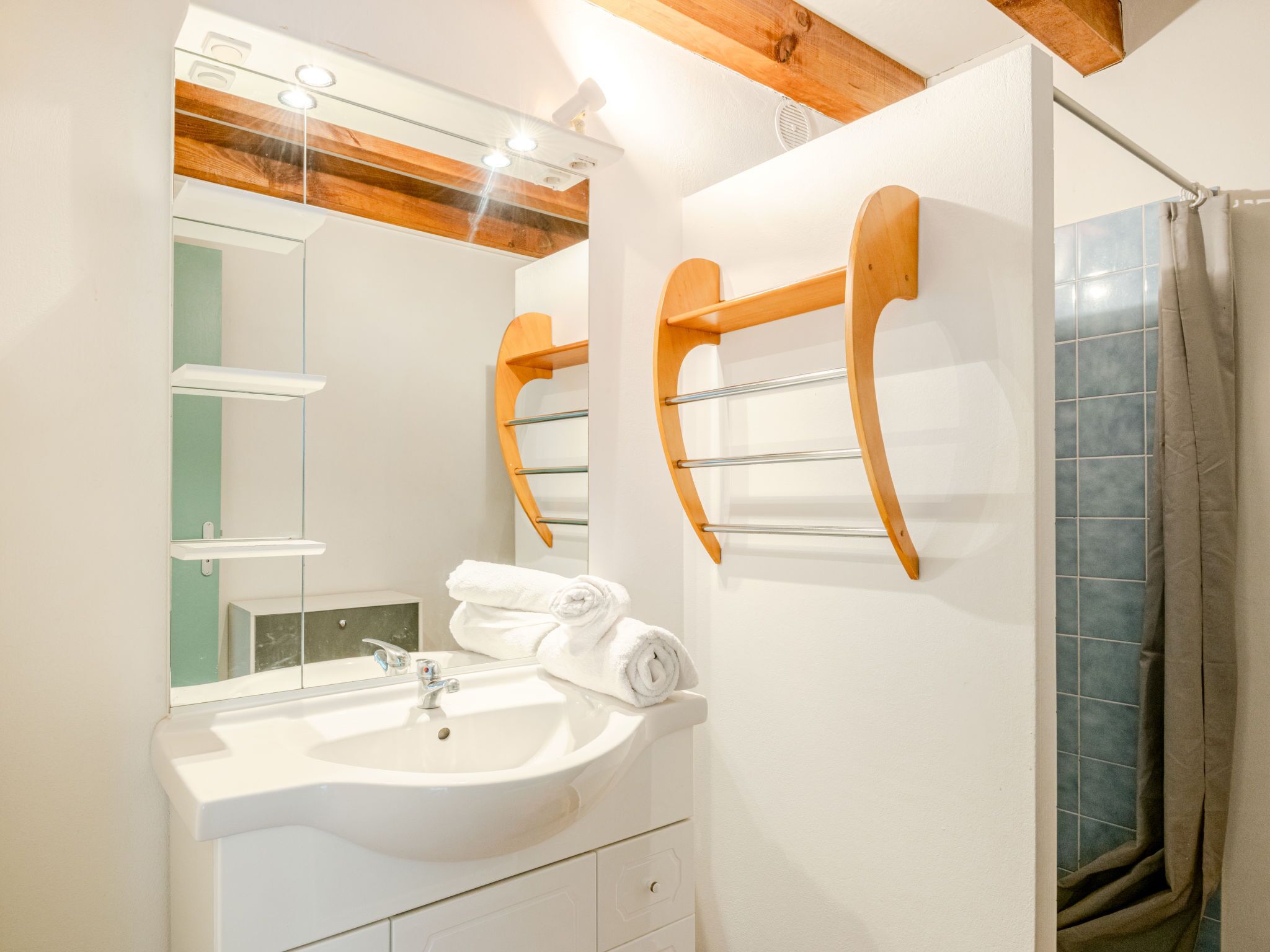 A bathroom with a white sink, wooden towel racks, a mirror, and a shower with a curtain.