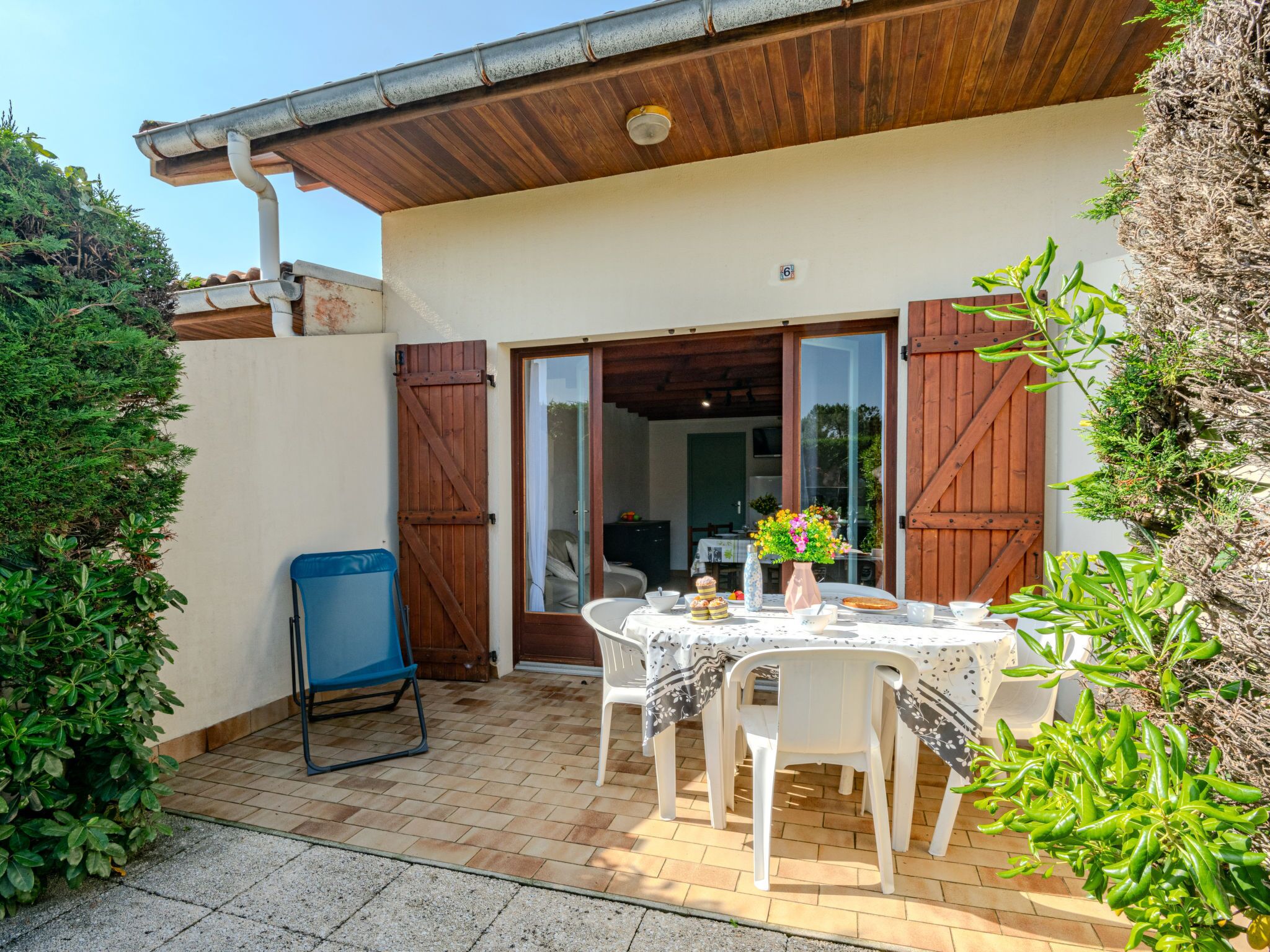Une terrasse avec une table dressée pour le repas, entourée de verdure et délimitée par une clôture en bois.