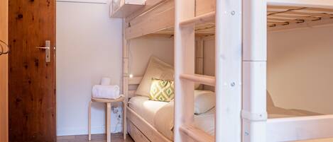 Une chambre avec des lits superposés, une porte en bois, une petite table avec une serviette et une illustration encadrée représentant un poisson accrochée au mur.