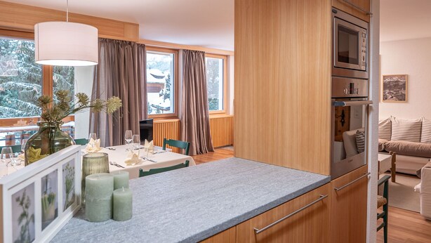 Une cuisine moderne avec des meubles en bois, un four encastré et un coin repas avec une table mise pour deux personnes.