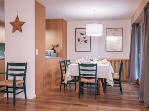 Een eethoek met een ronde tafel voor zes personen, omringd door zes groene stoelen. Er hangen kunstwerken in lijsten aan de muur, een ster decoratie aan de linkerkant, en een houten paneel op de muur.