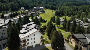 Un quartier résidentiel composé de plusieurs immeubles, dont un grand hôtel à étages avec de nombreux balcons, le tout entouré d’une végétation luxuriante et avec des montagnes en toile de fond.