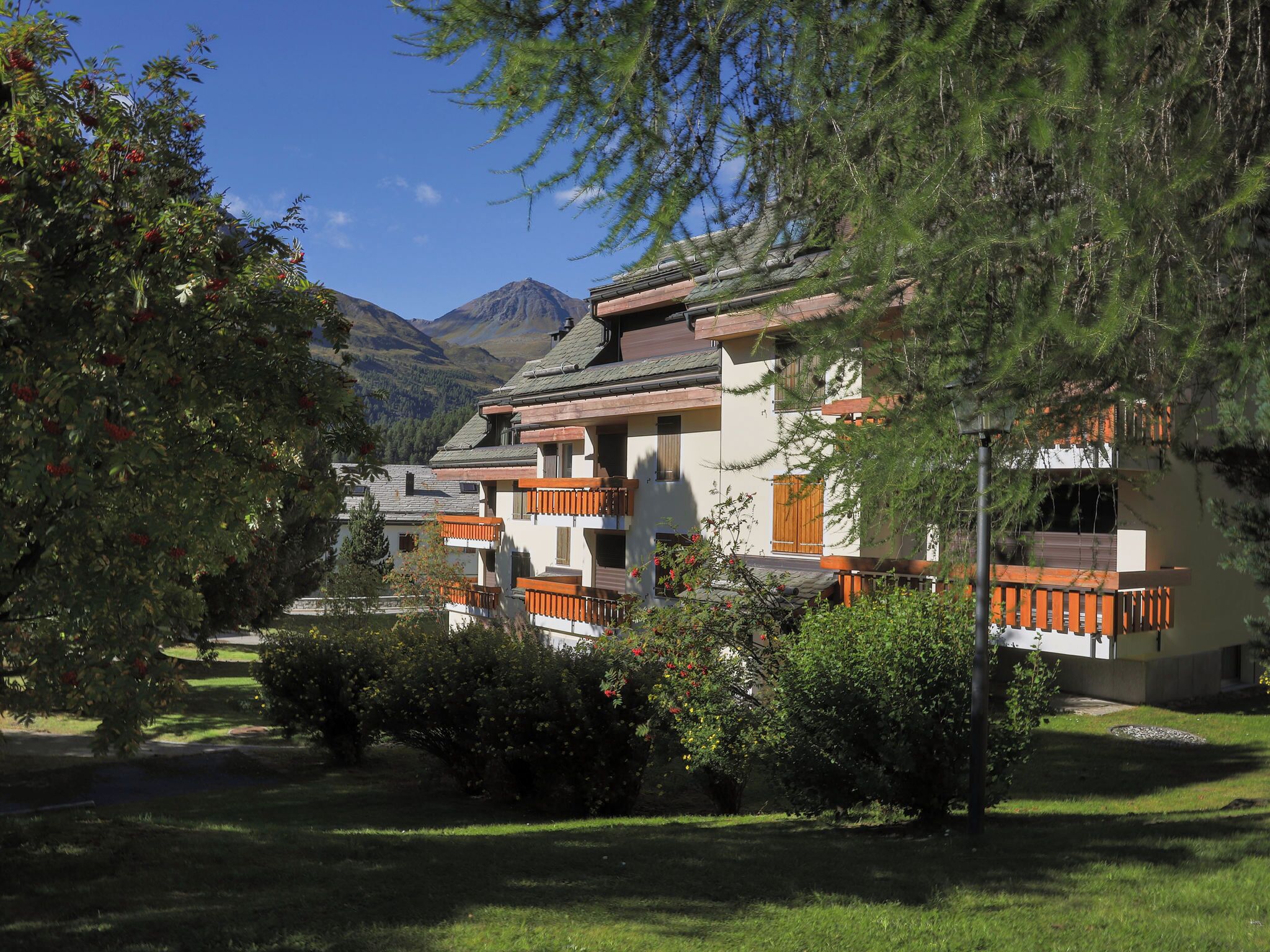 A traditional chalet-style building with multiple balconies, surrounded by lush greenery and a mountainous backdrop.