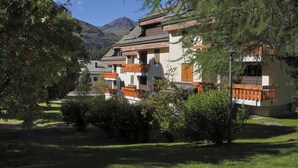Un bâtiment de style chalet traditionnel, doté de nombreux balcons et entouré d’une végétation luxuriante, avec une chaîne de montagnes en toile de fond.