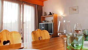 A dining area with a wooden table, chairs, and a television in the background. - Valetta Sura by Interhome (Flims)