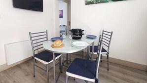 Ein Essbereich mit einem runden Tisch, vier Stühlen, einem an der Wand montierten Fernseher und einem Gemälde über dem Tisch.