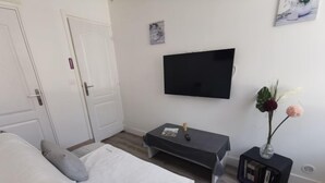 Ein modernes Schlafzimmer mit Bett, Nachttisch, Fernseher und einem kleinen Beistelltisch mit einer Vase.
